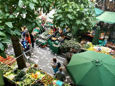 people standing near patio umbrella surrounded with fruits and vegetable stalls